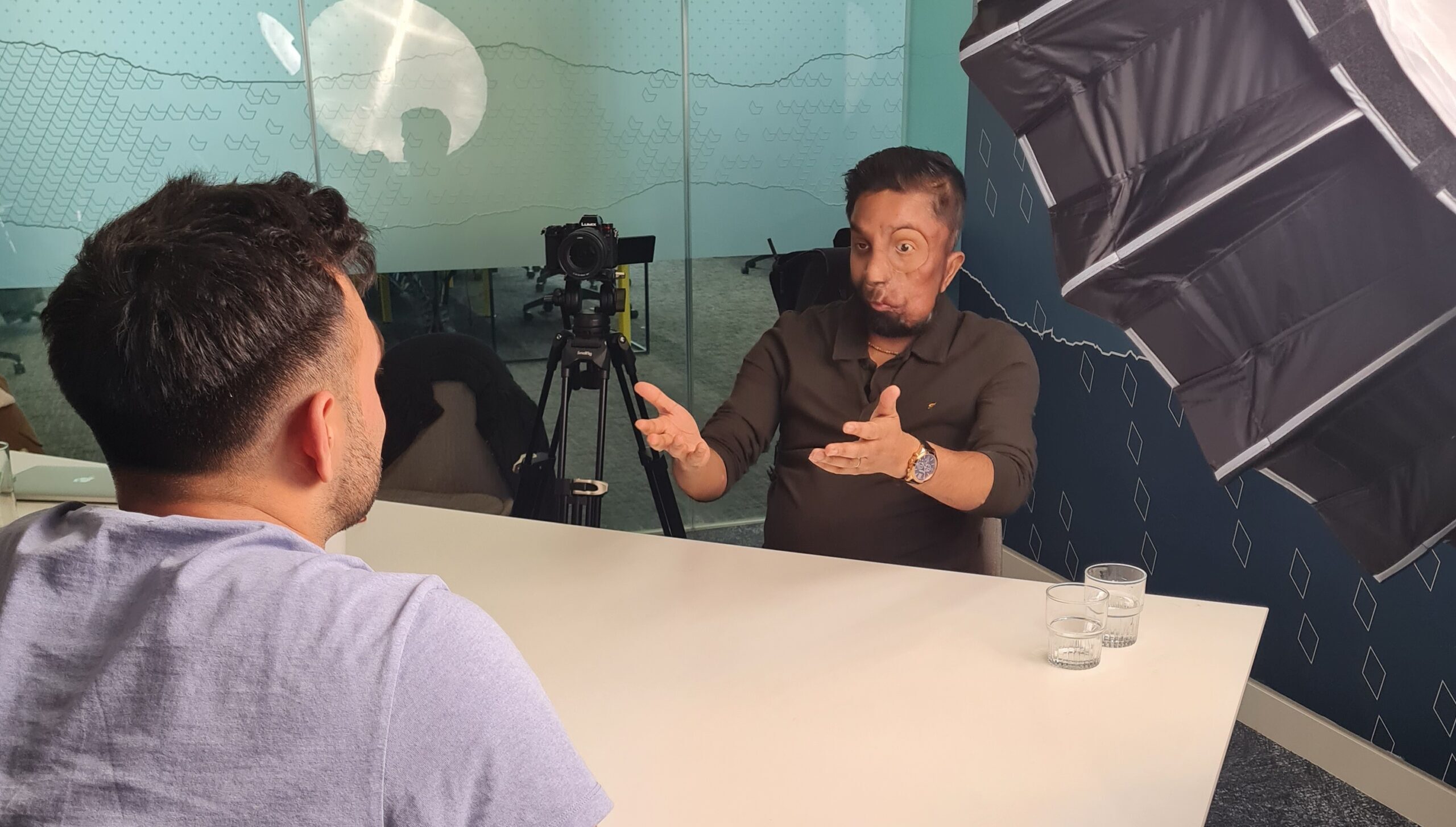 Krish and Amit sat at a table with a camera, during a Tales to Inspire filming day.